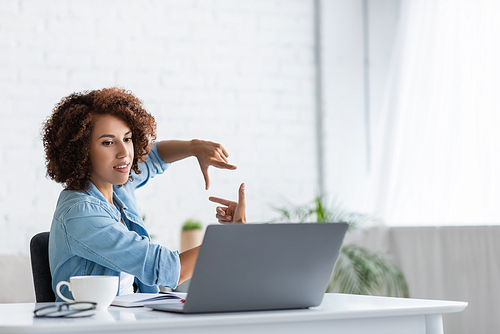 curly african american woman showing square shape with hands during video call on laptop