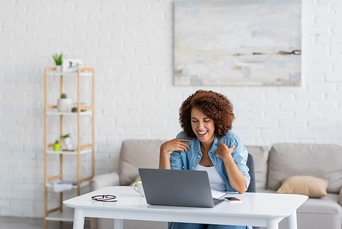 curly african american woman laughing during video call on laptop