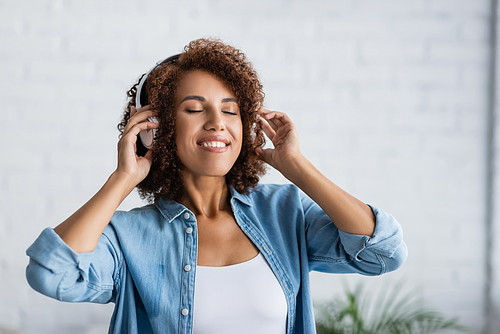 curly african american woman smiling while listening music in wireless headphones