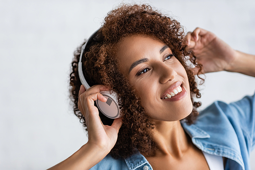 happy african american woman smiling while listening music in wireless headphones