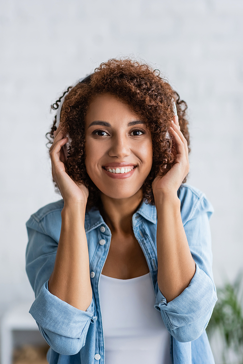 joyful african american woman smiling while listening music in wireless headphones