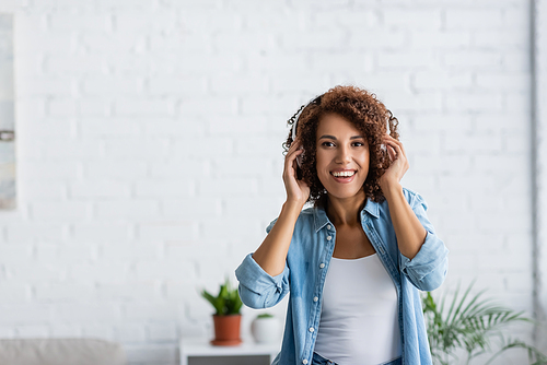 positive african american woman smiling while listening music in wireless headphones