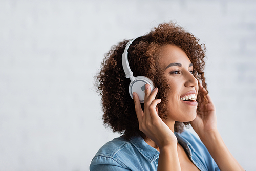 excited african american woman smiling while listening music in wireless headphones