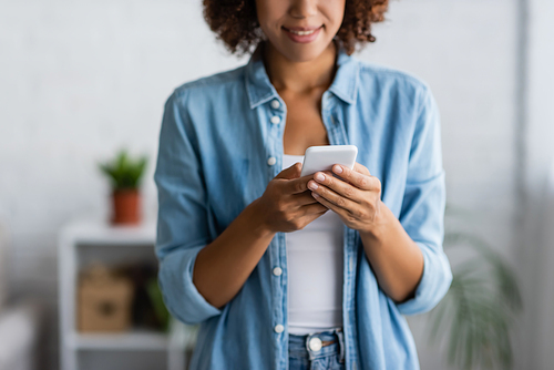 cropped view of curly african american woman smiling while messaging on smartphone