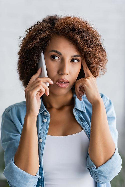 thoughtful african american woman talking on smartphone at home