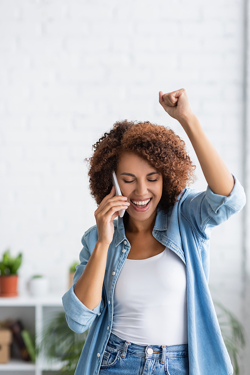 excited african american woman talking on smartphone and gesturing at home