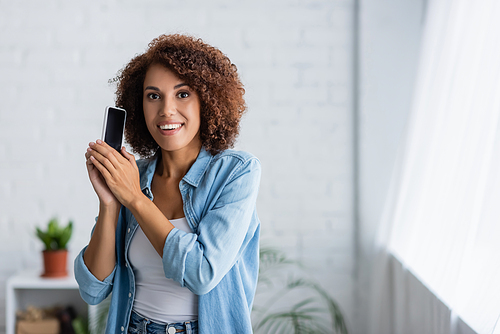 excited african american woman holding smartphone with blank screen and looking at camera