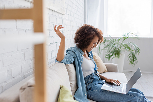 side view of cheerful african american woman using laptop while sitting on sofa and working from home