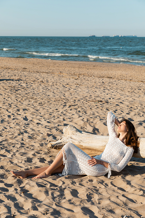 Woman in knitted dress lying near wooden log on beach