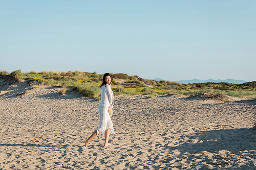 Happy woman holding straw hat and looking at camera on beach