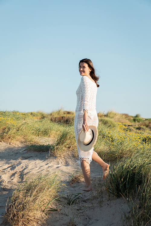 Young woman holding sun hat while walking on grass on beach