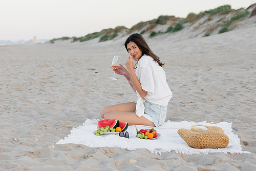 Brunette woman holding wife near fresh fruits and sunglasses on beach