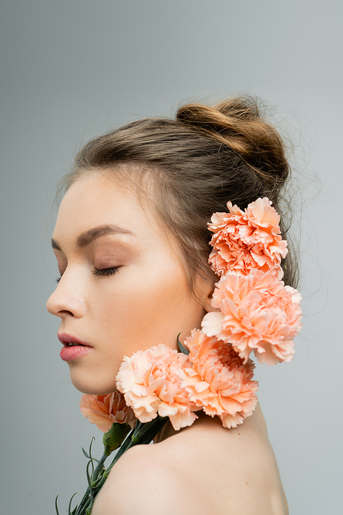 young woman with closed eyes and natural makeup near fresh carnations isolated on grey