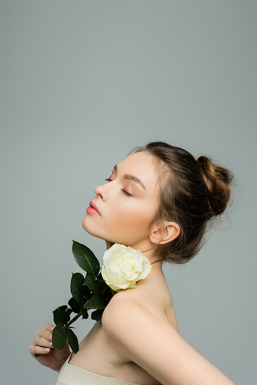 sensual woman with closed eyes holding fresh rose near naked shoulder isolated on grey