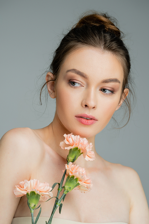 charming woman with naked shoulders and perfect skin posing with peach carnations isolated on grey