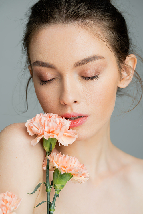 portrait of sensual woman posing with closed eyes near peach carnations isolated on grey
