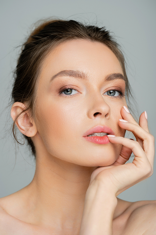 young and pretty woman with natural makeup posing with hand near face isolated on grey