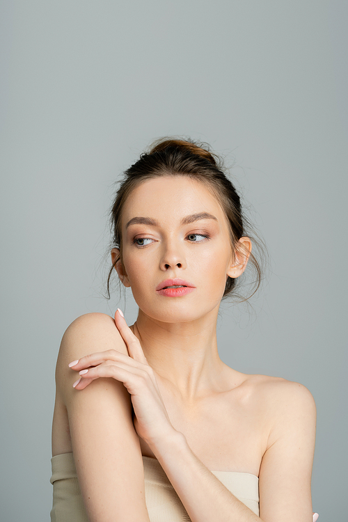 young woman with bare shoulders and natural makeup posing isolated on grey