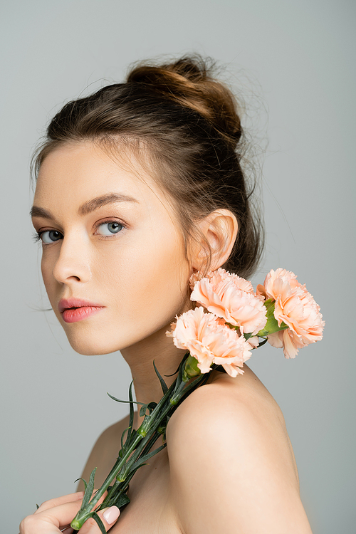 Young fair haired woman with naked shoulders holding carnations isolated on grey