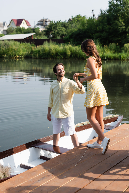 happy bearded man in summer clothes holding hands with girlfriend near boat