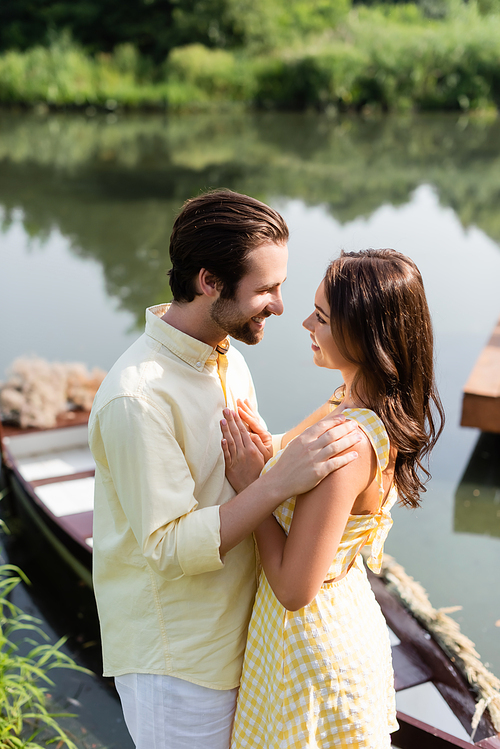 side view of happy couple looking at each other near blurred boat