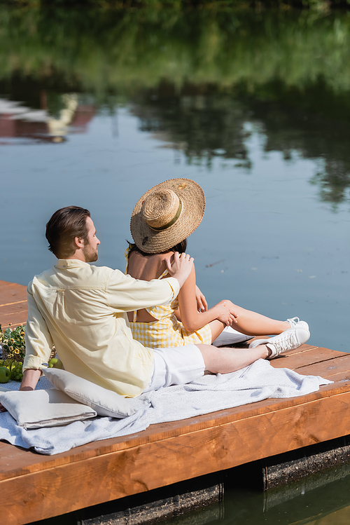 bearded man and woman in straw hat sitting on pier during picnic