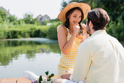 excited woman in straw hat holding glass of wine and looking at boyfriend