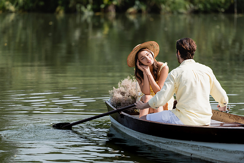 dreamy woman in straw hat looking at romantic boyfriend during boat ride