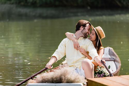 happy young woman in straw hat hugging man during romantic boat trip