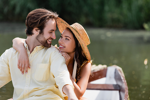 smiling young woman in straw hat hugging happy man during romantic boat trip