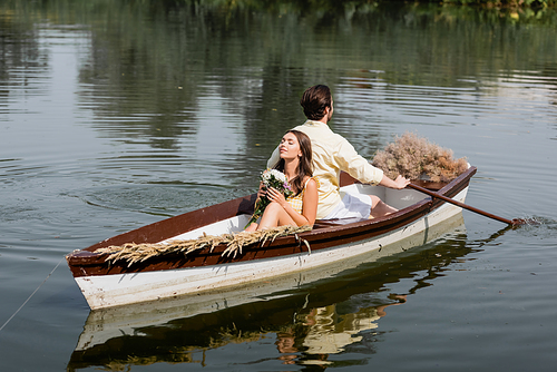 young woman holding flowers and leaning on back of boyfriend during romantic boat trip