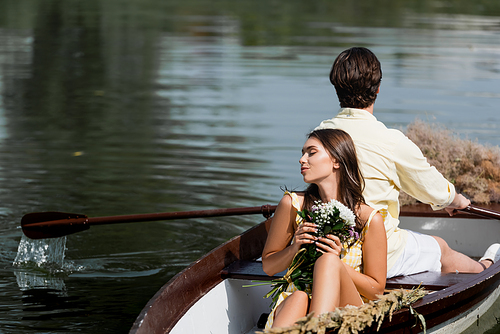 young woman holding flowers and leaning on back of man during romantic boat trip