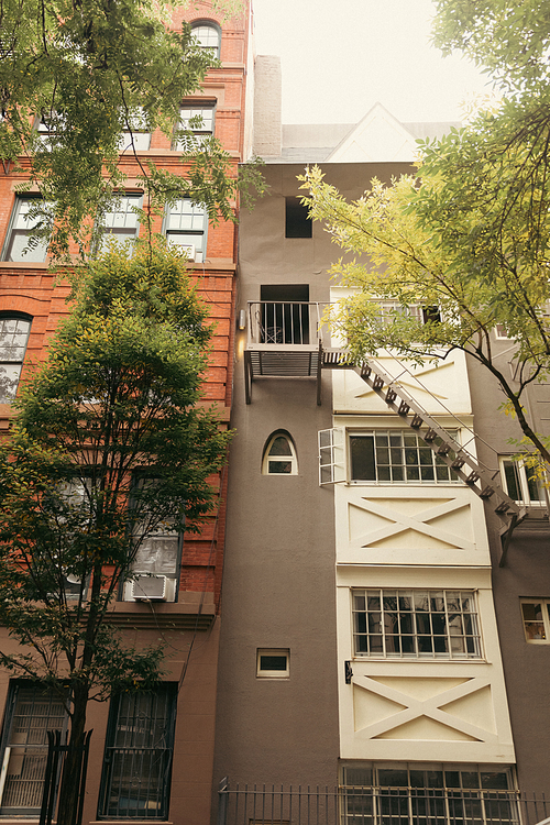 stone houses with windows and white balconies near autumn trees on urban street of New York City