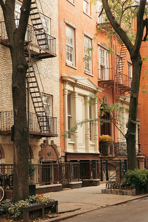 stone building with balconies and fire escape ladders near trees on sidewalk in New York City