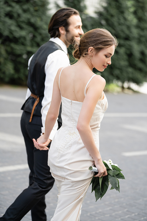 happy groom holding hand of gorgeous bride in white dress with wedding bouquet