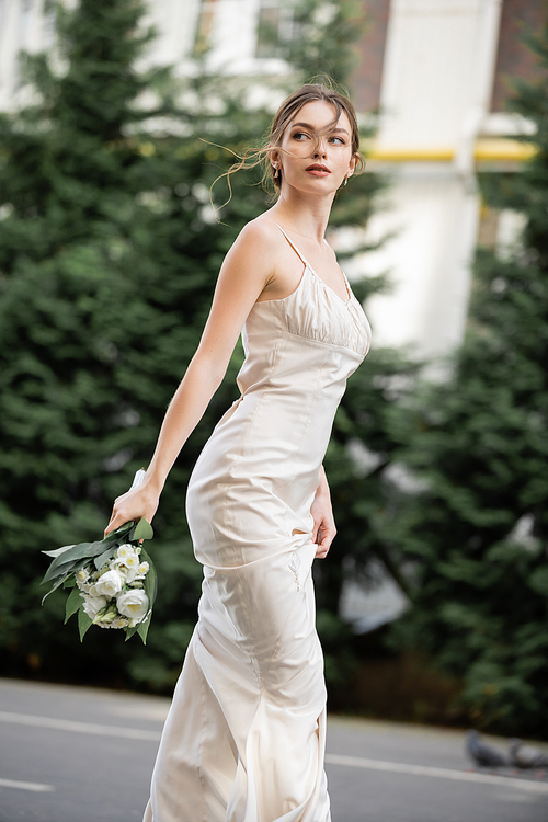 pretty woman in white dress holding wedding bouquet with blooming flowers