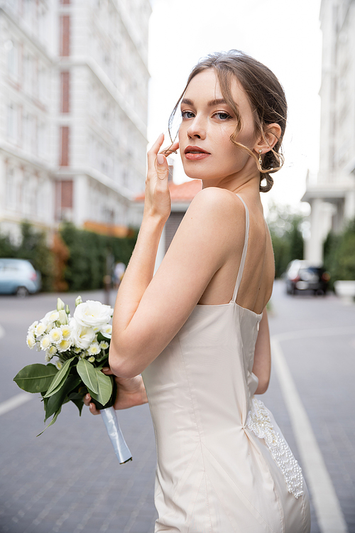 young woman in white dress holding wedding bouquet and looking at camera