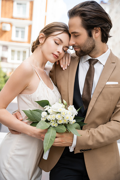 young bride in wedding dress holding bouquet and leaning on groom in suit