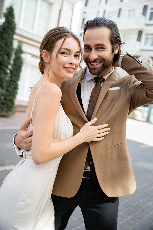 happy bride hugging bearded groom and smiling outside