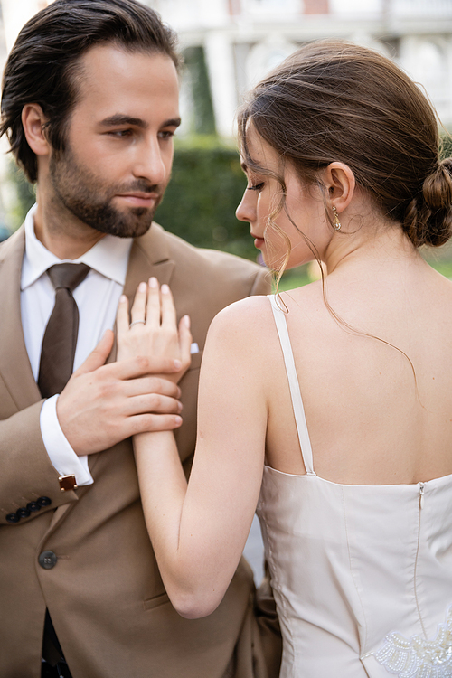 bearded man in suit with tie looking at pretty bride outdoors