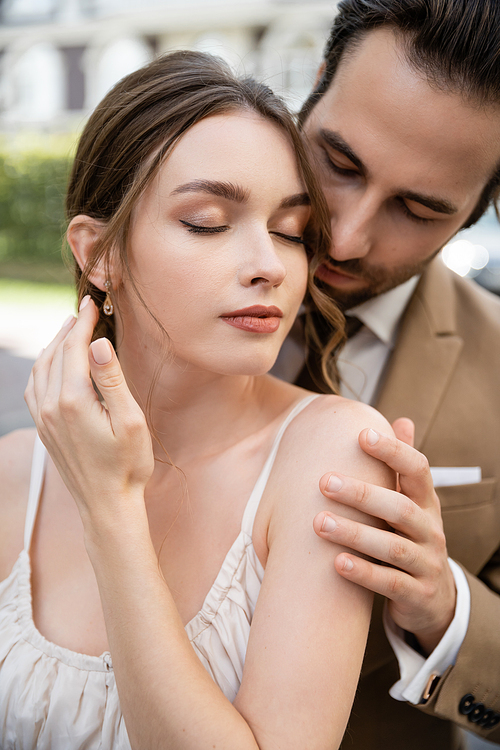 bearded man in suit with tie hugging pretty bride with closed eyes outdoors