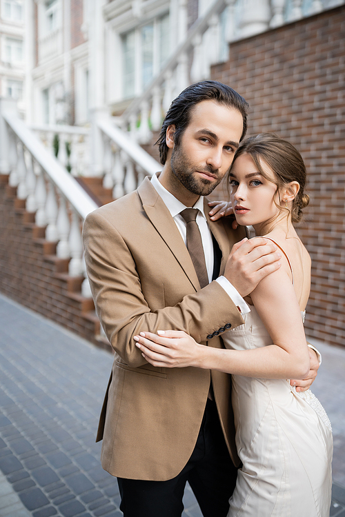 groom in beige suit hugging sensual bride in white wedding dress