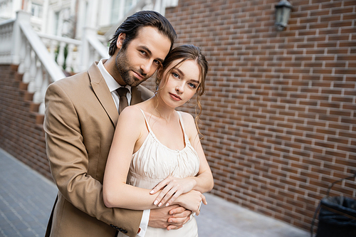 young groom in beige suit hugging gorgeous bride in white wedding dress