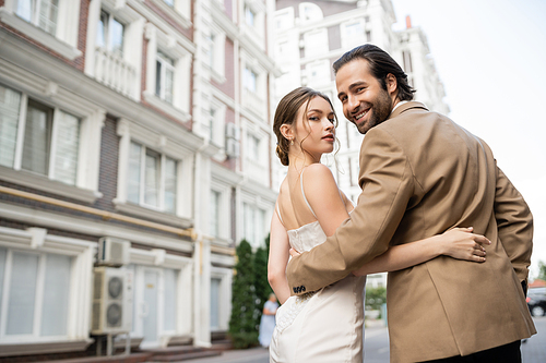 joyful groom in beige suit hugging gorgeous bride in white wedding dress