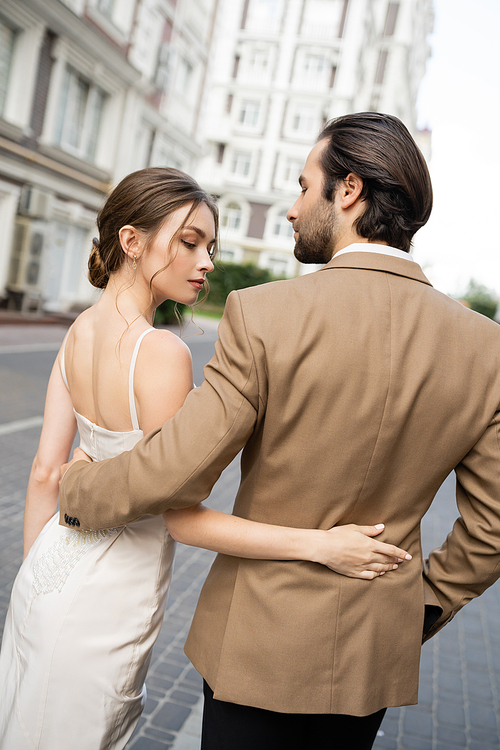 good looking groom in beige suit hugging gorgeous bride in wedding dress