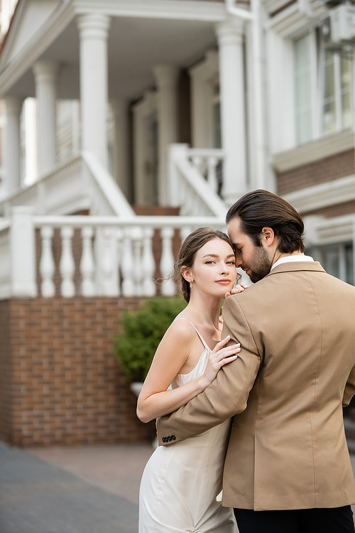 bearded groom in beige suit hugging charming bride in white wedding dress