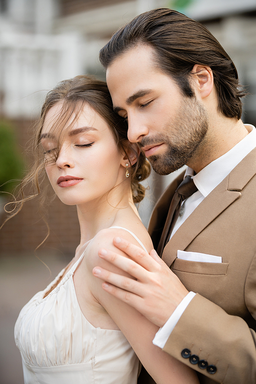 groom in beige blazer hugging gorgeous bride in white wedding dress