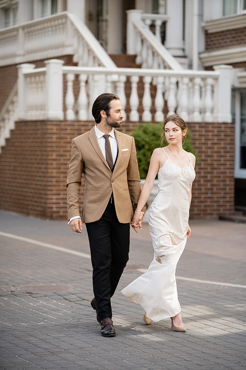 full length of bride in wedding dress holding hands with groom while holding hands on street