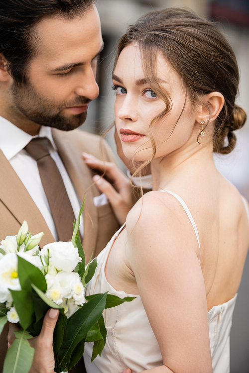 portrait of bride in wedding dress holding blooming flowers and hugging with groom