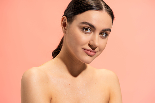 charming young woman with bare shoulders looking at camera isolated on pink